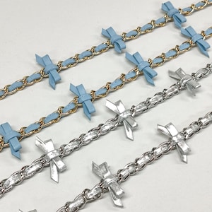K&ouml;nnte beinhalten: Nahaufnahme mehrerer dekorativer Ketten. Zwei Ketten haben ein goldfarbenes Kettenglied-Design mit hellblauen B&auml;ndern und Schleifen. Die anderen Ketten haben ein silberfarbenes Kettenglied-Design mit silbernen Schleifen.