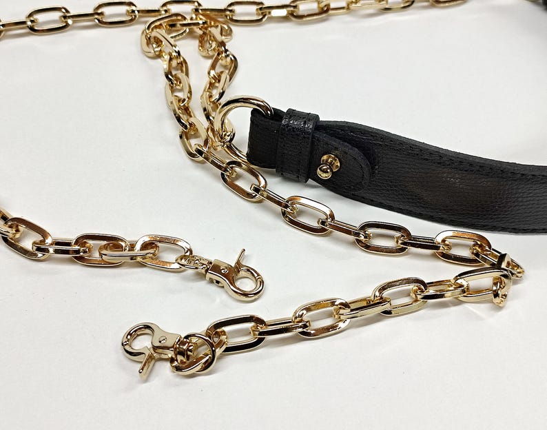 May include: Gold-colored chain straps and a black leather strap. The chains have a lobster clasp closure. The chains are made of metal and have a shiny finish. The black strap has gold-colored hardware.