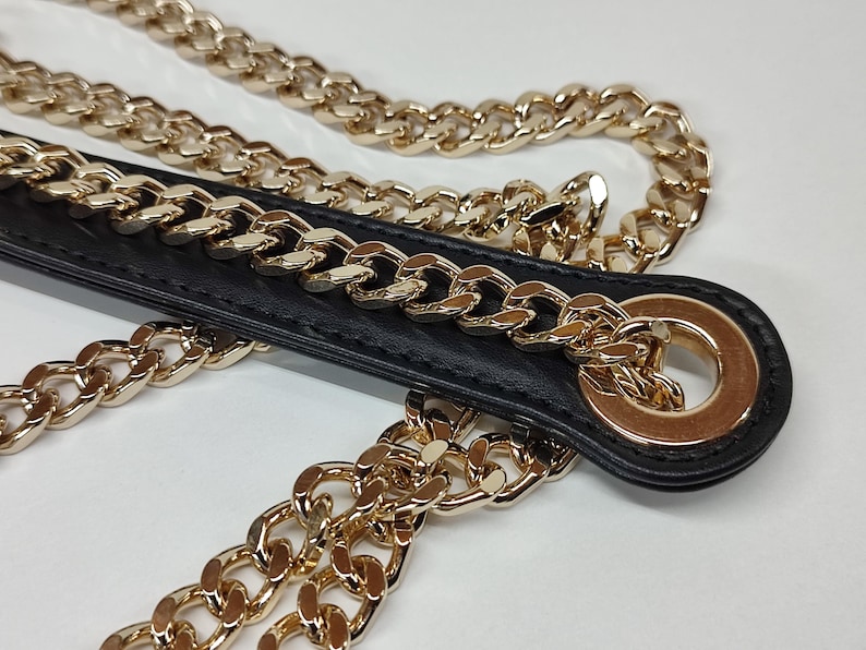 K&ouml;nnte beinhalten: Ein schwarzes Lederband mit einer goldenen Kette daran. Das Band hat einen goldenen Ring am Ende.