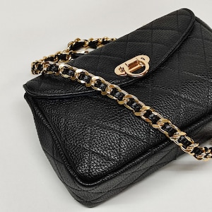 Puede incluir: Un bolso de hombro acolchado negro con una correa de cadena dorada y un cierre dorado.