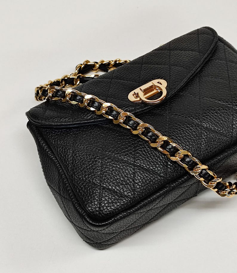 Puede incluir: Un bolso de hombro acolchado negro con una correa de cadena dorada y un cierre dorado.