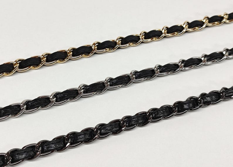 May include: Three metal chain straps for bags, each featuring a black leather or faux leather strip woven through the links. The top chain is gold-toned, the middle chain is silver-toned, and the bottom chain is a dark gunmetal-toned finish.