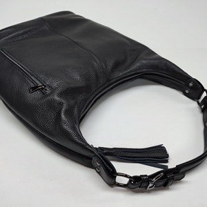 May include: A black hobo bag crafted from textured leather, featuring a top zipper closure, a side exterior zipper pocket, and an adjustable shoulder strap with metal hardware. A decorative leather tassel is attached to the side of the bag.