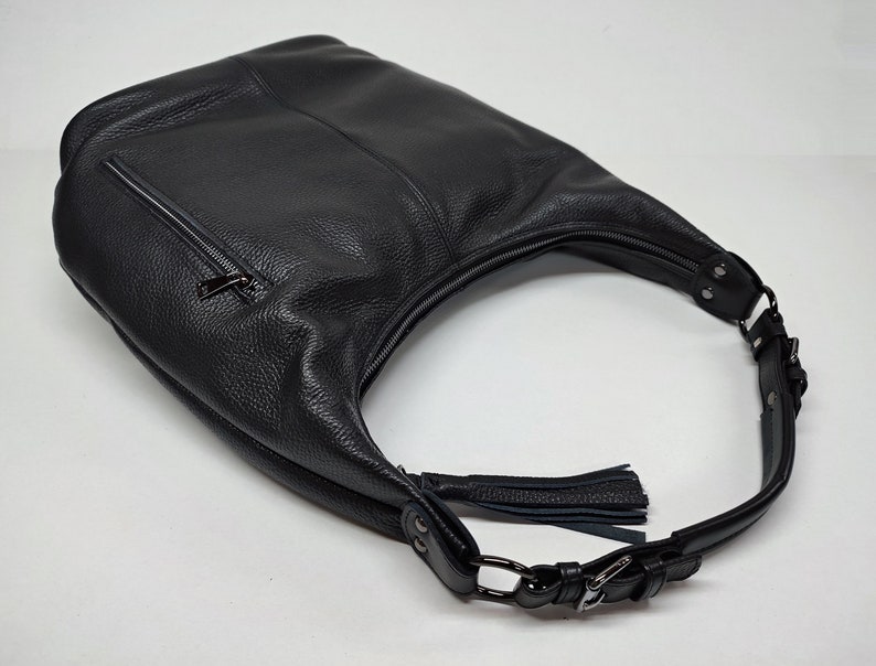 May include: A black hobo bag crafted from textured leather, featuring a top zipper closure, a side exterior zipper pocket, and an adjustable shoulder strap with metal hardware. A decorative leather tassel is attached to the side of the bag.