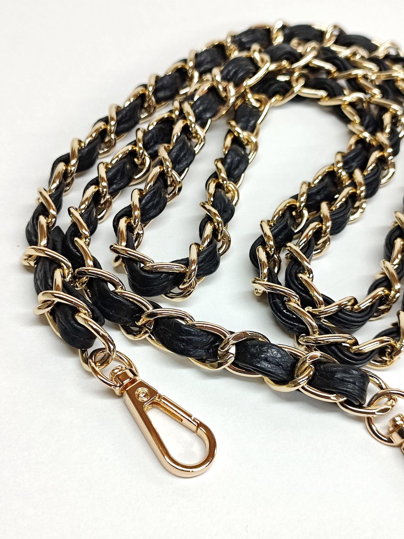 May include: A gold chain with black leather interwoven, featuring a gold clasp.