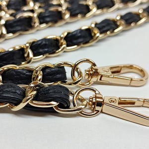May include: A black leather and gold chain strap with two gold clasps. The strap is designed for a handbag or purse.