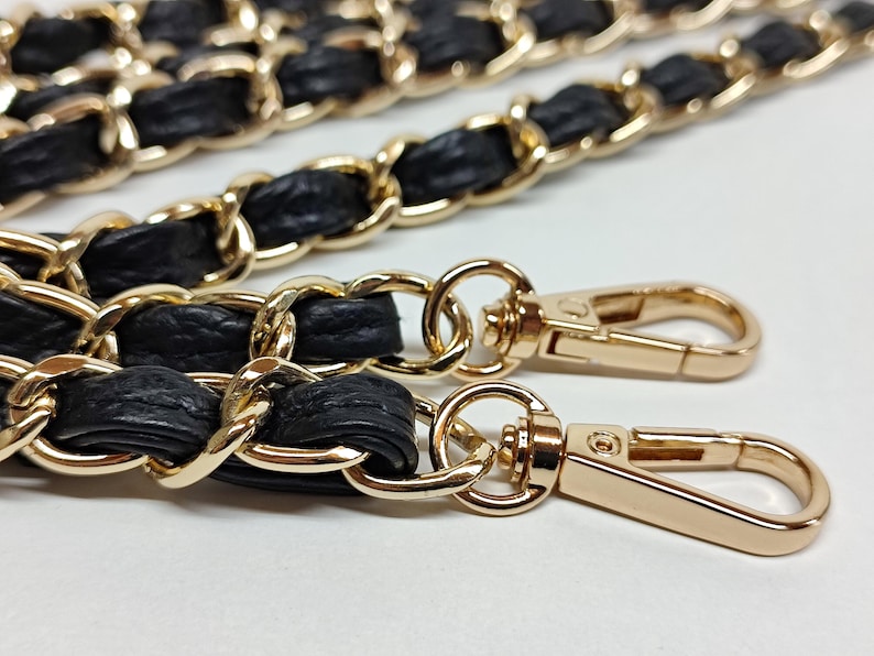 May include: A black leather and gold chain strap with two gold clasps. The strap is designed for a handbag or purse.