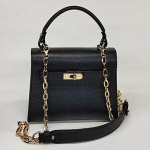 May include: Black handbag with a gold chain strap and handle. The bag has a rectangular shape with a flap closure and a gold clasp. The chain is draped over the front of the bag and can be used as a shoulder strap.