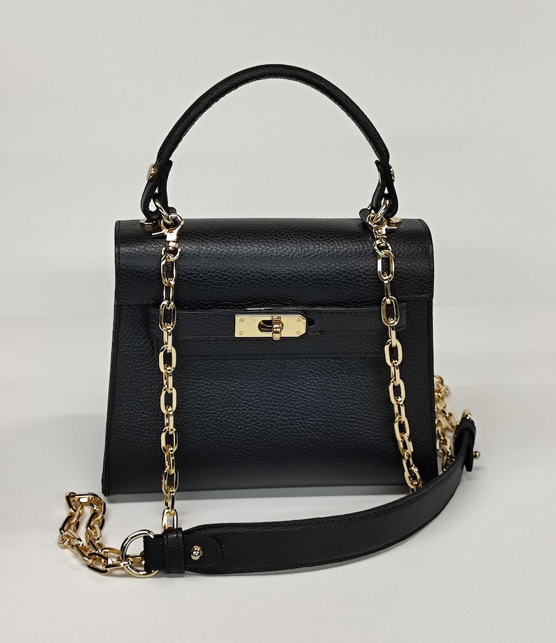 May include: Black handbag with a gold chain strap and handle. The bag has a rectangular shape with a flap closure and a gold clasp. The chain is draped over the front of the bag and can be used as a shoulder strap.