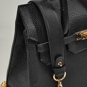 May include: Close-up of a black leather handbag with a textured finish. The bag features a gold-colored clasp and chain strap. The shoulder strap is also black leather.