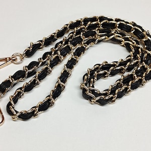 May include: Black and gold chain strap with two gold clasps. The chain is made of interwoven leather and metal.