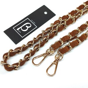May include: A brown suede and gold-tone metal chain strap for a handbag, featuring two lobster claw clasps at the ends. A black rectangular tag is included with the white text "B" and "est. 1983" printed inside a white square border.