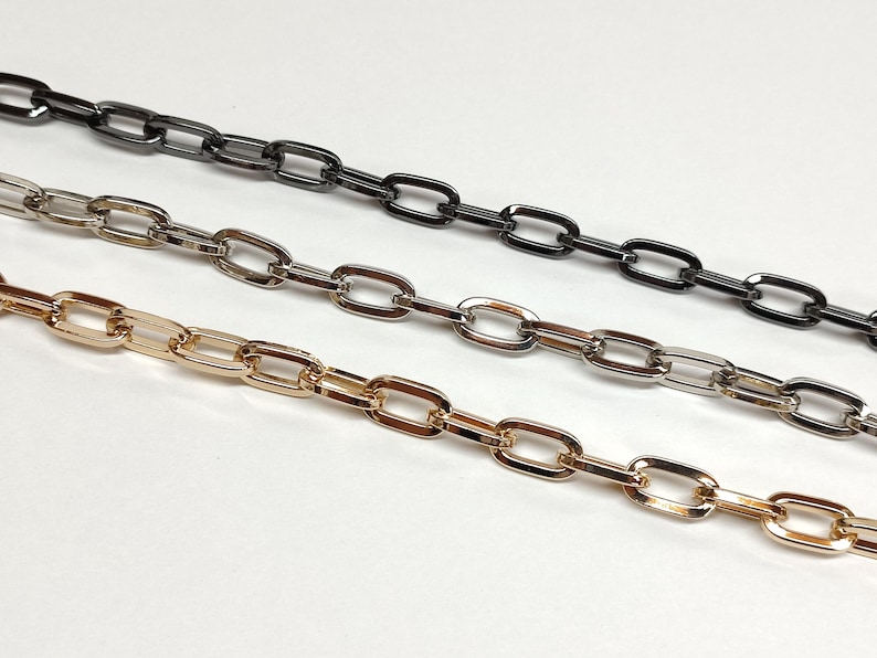May include: Three metal chain strands in gold, silver, and black. Each chain has an oval link design. The chains are arranged diagonally against a white background, showcasing their color variations and link style.