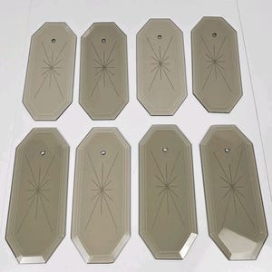 May include: A set of eight octagonal smoked glass wall mirror panels, each featuring a bevelled edge and a central etched starburst pattern. Every panel includes a single small circular mounting hole positioned near the top centre section.