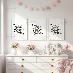 May include: Three white framed art prints with the text "Your Design Here" are displayed above a white dresser. The dresser is decorated with pink flowers, stuffed bunnies, and a fairy figurine. A garland of pink and white circles hangs above.