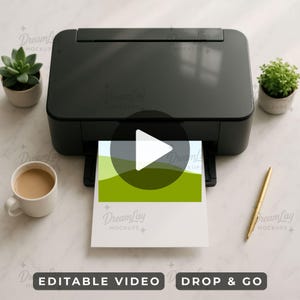 Op de afbeelding: Een zwarte printer met een afgedrukte afbeelding van een groen landschap. De afbeelding staat op wit papier. Een gouden pen, een kopje koffie en twee kleine planten in potten staan op het witte oppervlak.