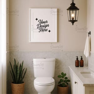 Puede incluir: Un interior de baño con un marco blanco con el texto "Your Design Here". Una linterna negra cuelga sobre un inodoro blanco. Una cesta tejida contiene una planta de serpiente y una pequeña planta está en una cesta. Dispensadores de jabón marrones en el mostrador.