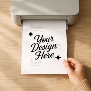 May include: A white printer is shown with a printed sheet of paper emerging. The paper has the text "Your Design Here" in a stylish black font. The image is set on a light wood surface.