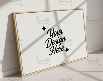 May include: A rectangular canvas with a light wood frame, leaning against a white wall. The canvas displays the text "Your Design Here" in a stylish black script. The scene is illuminated by natural light, creating shadows.