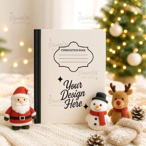 Puede incluir: Un cuaderno de composición con el texto "Your Design Here" y "Composition Book" está rodeado de decoraciones navideñas. Un Papá Noel, un muñeco de nieve y un reno se colocan frente al libro sobre una manta de punto blanca.