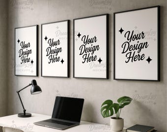 May include: Four black framed art prints with white backgrounds and the text "Your Design Here" are displayed on a gray wall. A desk with a laptop, lamp, plant, and books is in front of the prints.