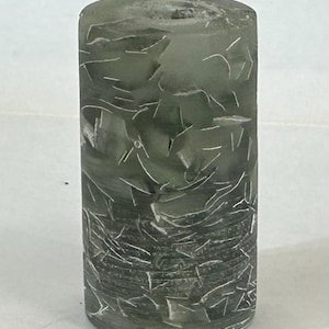 May include: A cylindrical, translucent object with a mottled green appearance. The surface is marked with white, linear patterns, creating a textured effect. The object has a rounded top and a slightly darker base.