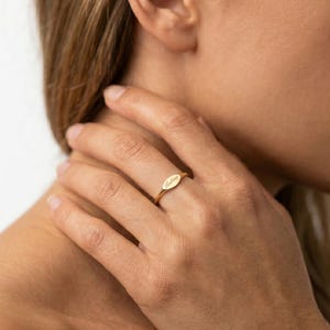 May include: A gold-toned ring featuring a slim, polished band and a small, oval-shaped flat plate at the center. The oval plate is engraved with the cursive script text 'Lindsey' in a delicate, dark font, creating a subtle and refined appearance.