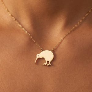 Peut inclure: Un collier doré avec un pendentif en forme de kiwi. Le pendentif est une silhouette stylisée de l'oiseau avec un long bec et de petits pieds. La chaîne du collier est délicate et également dorée.