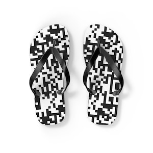 Op de afbeelding: Een paar witte teenslippers met een zwart-wit pixelpatroon. De slippers hebben zwarte bandjes en staan tegen een witte achtergrond. Ideaal voor casual gebruik.