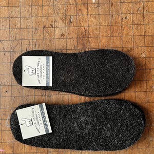 May include: Two pairs of black alpaca wool insoles. The insoles are made in the USA with US grown alpaca. The label reads "Mother Nature's Finest Fiber USA Alpaca Made in the USA with US Grown Alpaca."