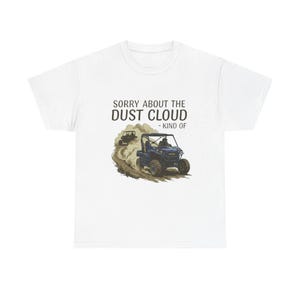 May include: White t-shirt featuring a graphic of two off-road vehicles kicking up dust. The text "SORRY ABOUT THE DUST CLOUD - KIND OF" is printed above the vehicles. The design is in shades of brown, black, and blue.