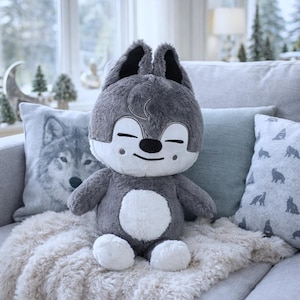 May include: A soft wolf toy with a smiling face, grey fur, and a white belly sits on a grey sofa. Decorative cushions with wolf designs and a faux fur throw are also present. The setting is a cosy, well-lit room.