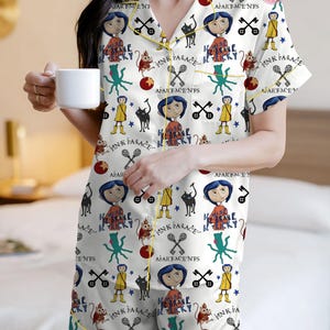 May include: White pajama set with a repeating pattern of cartoon characters, keys, and text. The set includes a short-sleeved top and shorts, trimmed with yellow piping. The pajama top has a button-down front. The person is holding a white mug.