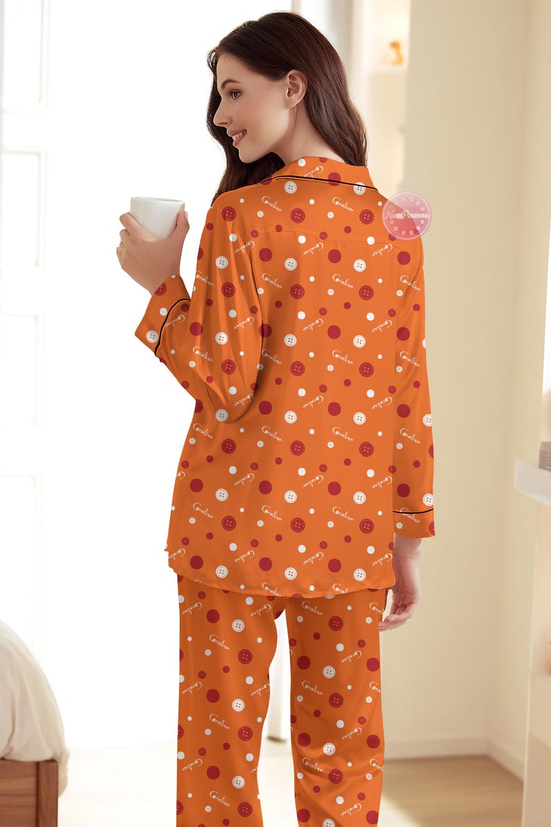 May include: Orange pajama set with a button and polka dot pattern. The long-sleeved top and pants feature a repeating design of white and red circles, and white buttons. The pajamas have black trim.