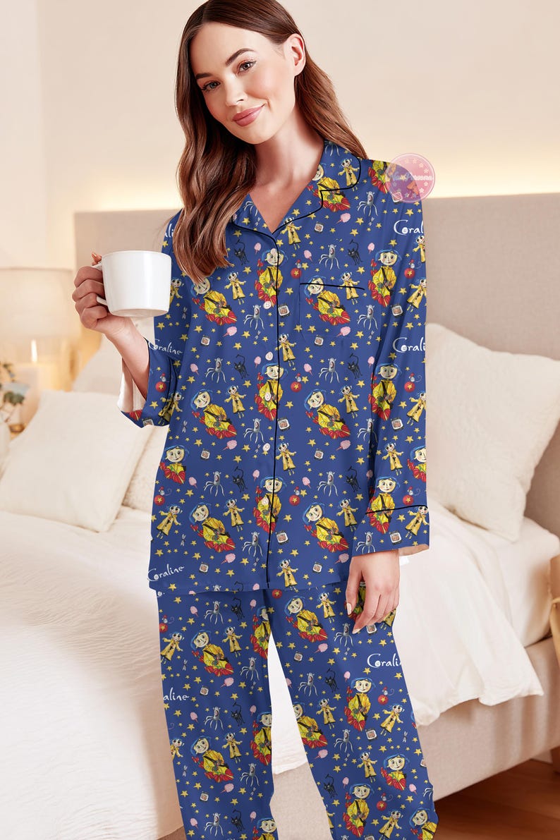 Peut inclure: Ensemble de pyjama bleu avec un motif r&eacute;p&eacute;t&eacute; de personnages de dessins anim&eacute;s, d'&eacute;toiles et le nom "Coraline". Le haut &agrave; manches longues et le pantalon sont en mati&egrave;re douce. La personne sur l'image tient une tasse blanche.