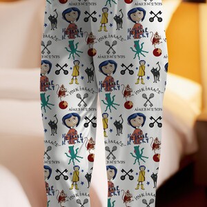 May include: White pajama pants with a repeating pattern featuring cartoon characters, text, and various symbols. The design includes a girl with blue hair, a black cat, keys, and the words "PINK PALACE" and "BE BRAVE BE TRICKY".