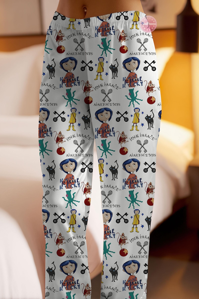 May include: White pajama pants with a repeating pattern featuring cartoon characters, text, and various symbols. The design includes a girl with blue hair, a black cat, keys, and the words "PINK PALACE" and "BE BRAVE BE TRICKY".