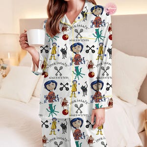 May include: White pajama set with a repeating pattern of cartoon characters, black cats, keys, and text. The pajamas have yellow trim and are worn by a person holding a white mug.