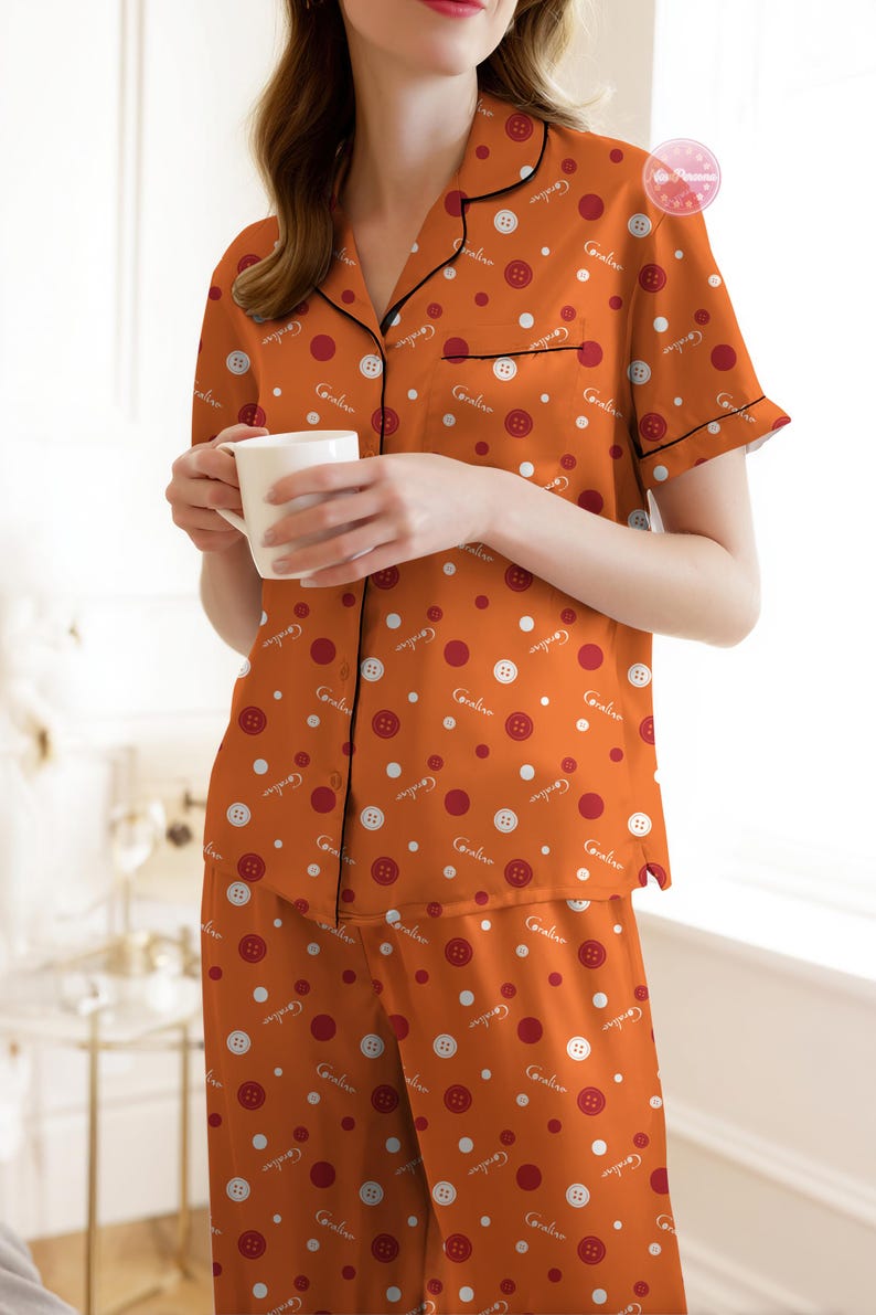 May include: Orange pajama set with a button and polka dot pattern. The short-sleeved top has black trim and a front pocket. The matching pants are a wrap style. The pajamas are made of a soft material.