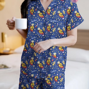 Peut inclure: Ensemble de pyjama bleu marine avec un motif r&eacute;p&eacute;t&eacute; d'un personnage de dessin anim&eacute;, d'&eacute;toiles et du mot "Coraline". Le haut &agrave; manches courtes et le short ont une bordure noire. Une tasse blanche est tenue.