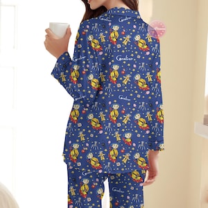 Peut inclure: Ensemble de pyjama bleu avec un motif r&eacute;p&eacute;t&eacute; d'un personnage, d'&eacute;toiles et du mot "Coraline". Le haut &agrave; manches longues et le pantalon ont une bordure noire. La personne sur l'image tient une tasse blanche.