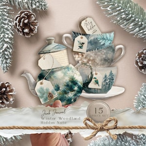 May include: A Winter Woodland themed junk journal set featuring a teapot and teacups with forest and nature designs. The set includes tags with the words "My Hidden Notes". The image also includes pinecones and frosted branches. The set is a 15-piece set.