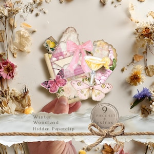 May include: A decorative paperclip set featuring a pink bow, a yellow cocktail glass with a lemon slice, and two butterflies in shades of pink and cream. The set includes nine pieces and extras, with text reading Winter Woodland Hidden Paperclip.