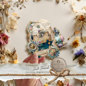 Peut inclure: Un trombone caché pour journal intime sur le thème steampunk avec un design de train. Le trombone présente des engrenages, un moteur bleu sarcelle et une esthétique vintage. L'image comprend le texte "Cosmos Junk Journal Hidden Paperclip" et une étiquette "6 Piece Set + extras."