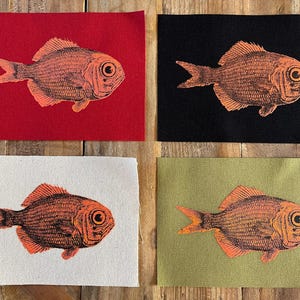 May include: Four fabric patches with a fish illustration. Each patch features a detailed orange fish design on a different background: red, black, white, and olive green. The patches are rectangular and appear to be made of canvas.