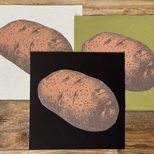 May include: Three art prints featuring a detailed illustration of a potato. The potato is rendered in shades of brown and tan, with a textured appearance. The prints are set against backgrounds of white, black, and olive green, creating a striking contrast.