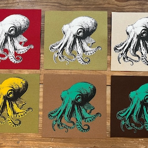 Puede incluir: Seis impresiones artísticas cuadradas con ilustraciones de pulpos en varios colores. Los pulpos son blancos, amarillos y turquesas, sobre fondos rojos, verdes, beige y marrones. Las impresiones están dispuestas sobre una superficie de madera.