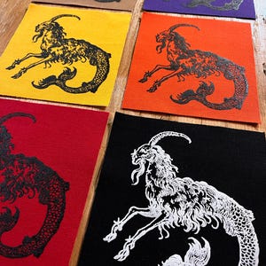 May include: A collection of six square fabric patches featuring a screen-printed Capricorn sea-goat illustration. The patches come in various colors including tan, purple, yellow, orange, red, and black, with contrasting ink colors for the design.