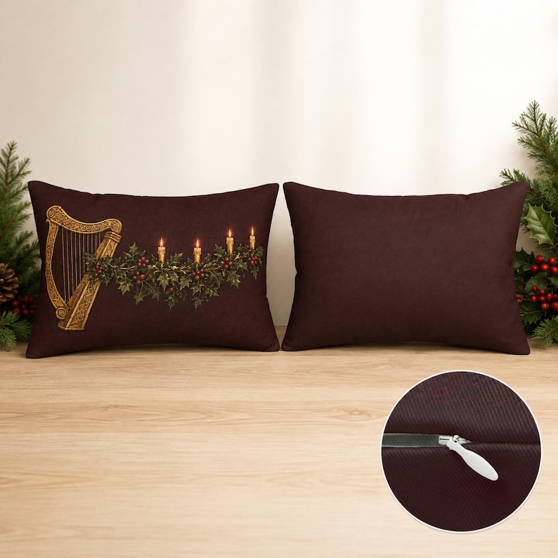 May include: Two rectangular dark brown throw pillows. The left pillow features a gold harp, green holly leaves, red berries, and four lit candles. The right pillow is solid dark brown. A circular inset shows a close-up of a white zipper closure.