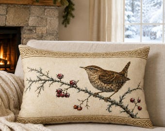 May include: A rectangular throw pillow with a beige background featuring a brown wren perched on a thorny branch with red berries. The pillow has a decorative border with a woven knot pattern along the top and bottom edges of the fabric.